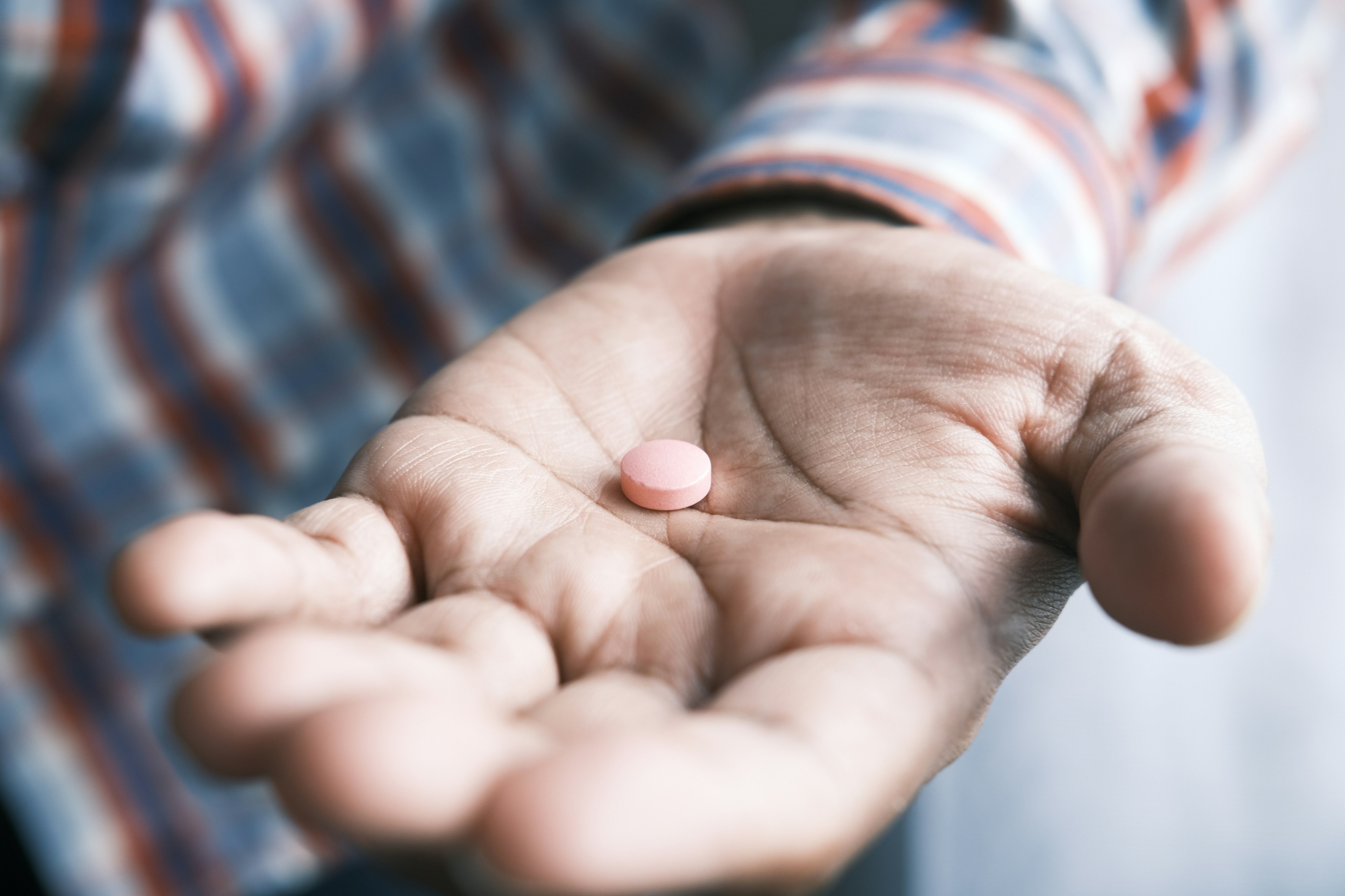Prescription pill in the palm of a masculine hand.