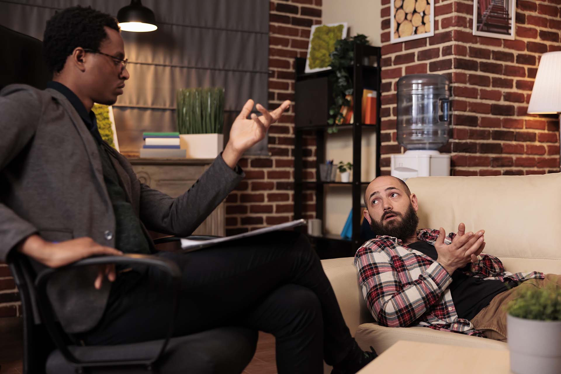 Caucasian man talking to male counselor about psychological issues, laying on couch at therapy session. Receiving counseling advice and support from therapist, doing psychoanalysis.